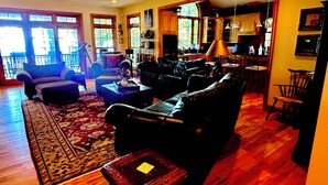 A spacious living room with a large window, a ceiling fan, and a view of the kitchen. - WNC’s Breathtaking Blue Ridge & Great Smokies meet the SC Jocassee Gorges (Rosman)