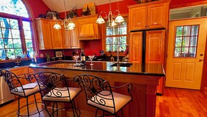 A kitchen with wooden cabinets, a large island with bar stools, and a refrigerator. - WNC’s Breathtaking Blue Ridge & Great Smokies meet the SC Jocassee Gorges (Rosman)