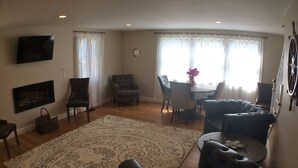 Een woonkamer met een groot, patroonrijk vloerkleed, leren banken, een eettafel met stoelen en een flatscreen televisie aan de muur.