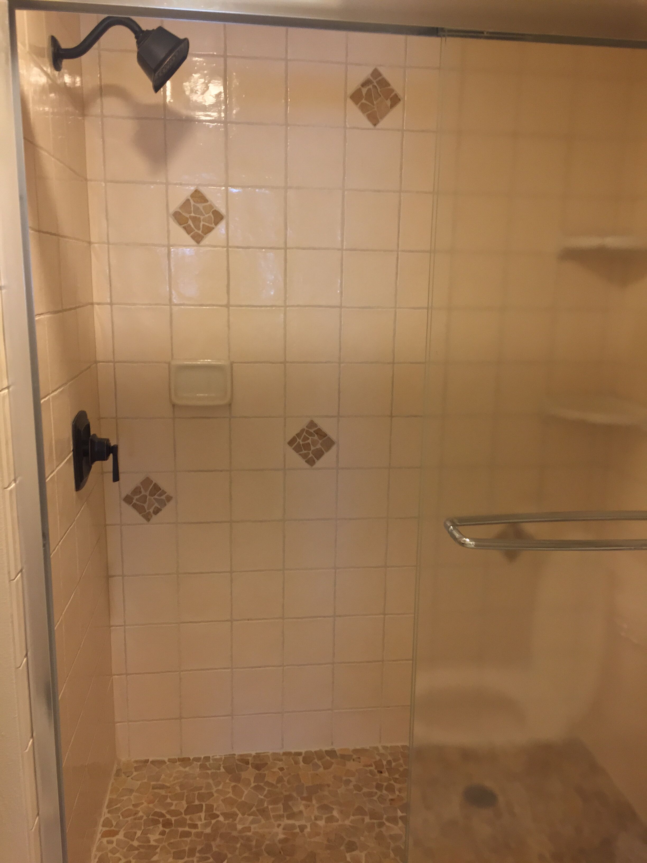 A shower with a handheld showerhead, a soap dispenser, and a glass door.