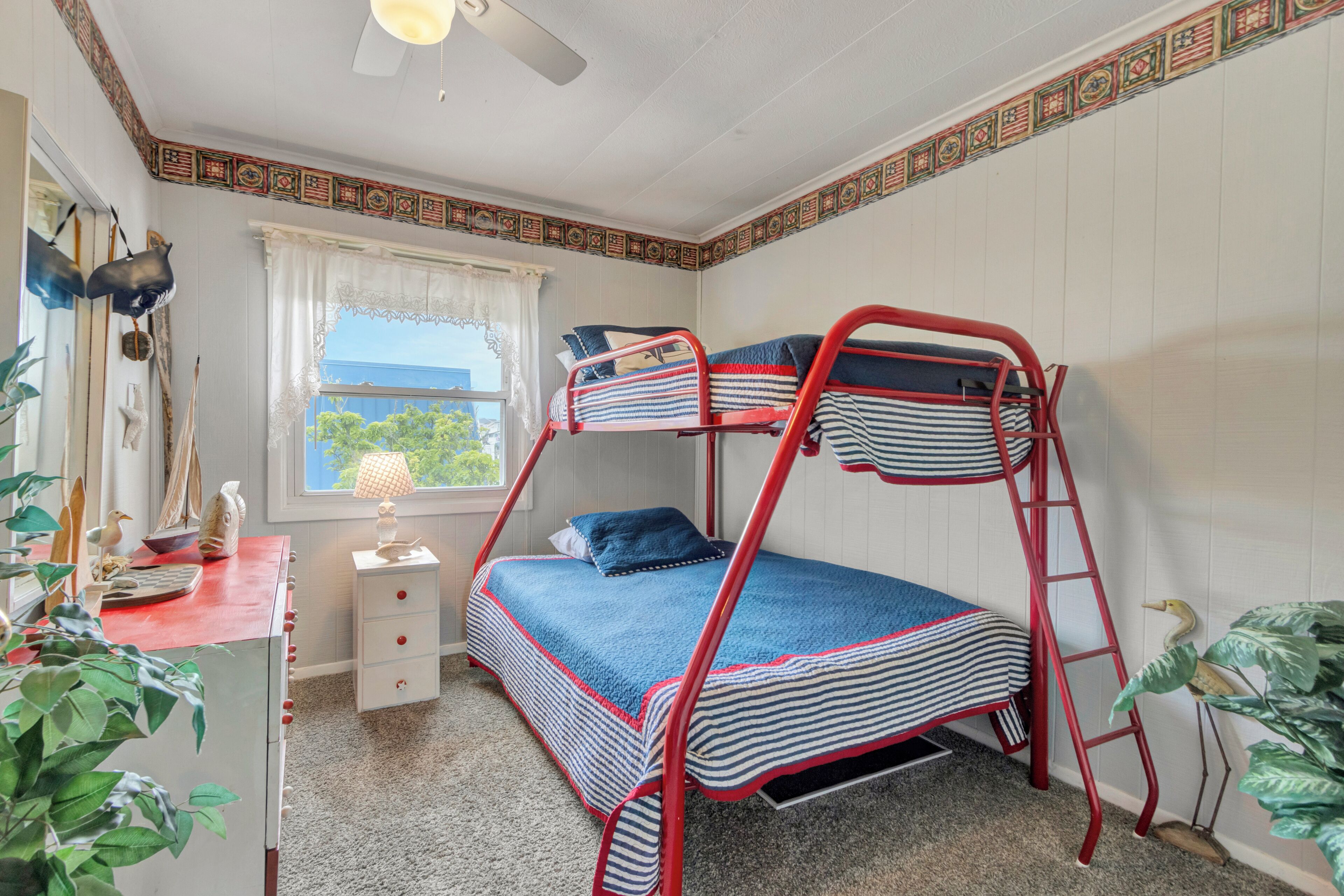 A bunk bed room with a window, a desk with a lamp, and a dresser.