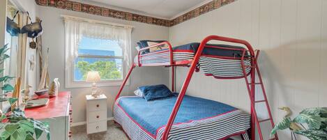 A bunk bed room with a window, a desk with a lamp, and a dresser.
