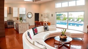 Un salon moderne avec un canapé blanc aux lignes courbes, une table basse et une vue sur une piscine.
