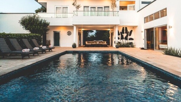 Une maison moderne à deux étages avec une piscine en premier plan.