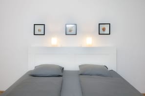 Un lit double avec une literie grise, une tête de lit blanche et trois tableaux encadrés accrochés au mur.