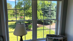 A room with a large window, a lamp on a table, and a chair with a decorative pillow. - Lovely house with gorgeous marsh views! (Wells)