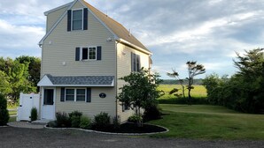 A two-story house with a gabled roof, a front porch, and a well-maintained lawn. - Lovely house with gorgeous marsh views! (Wells)