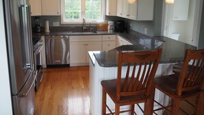 A modern kitchen with stainless steel appliances, white cabinets, a large window, and wooden chairs. - Lovely house with gorgeous marsh views! (Wells)