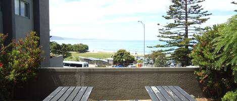 A view from a balcony overlooking a beach, with a parking area and a bus visible in the distance.