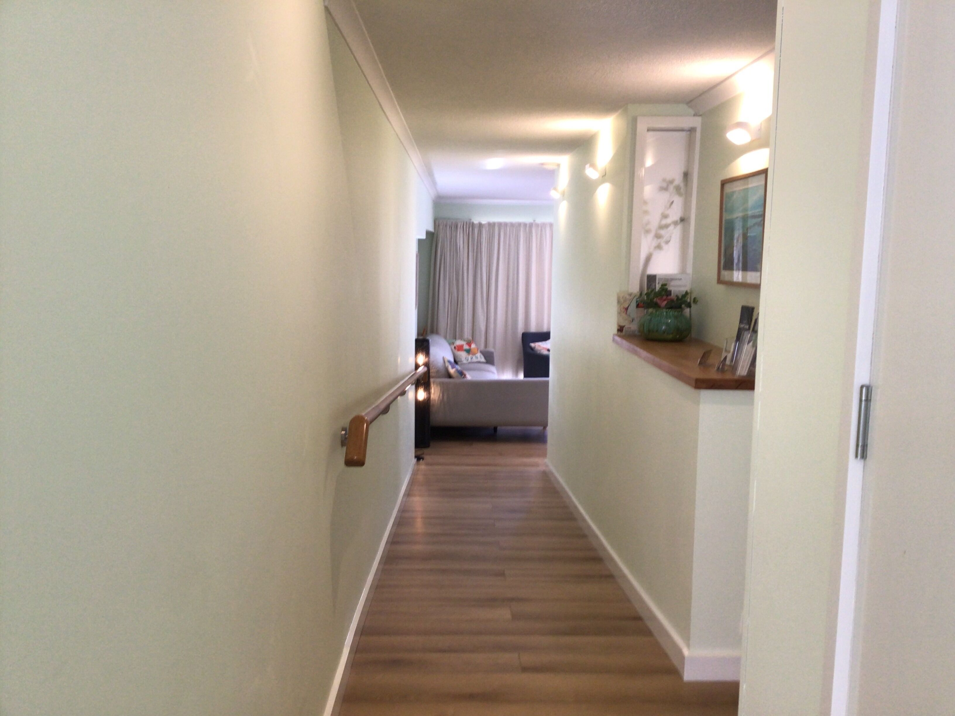 A narrow hallway with wooden flooring, a handrail on the left, and a door on the right.