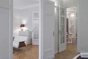 A modern hotel room with a bed, bedside table, lamp, and a view into the dining area. - Premium Suite in the Center, 2 BR, 2 BA, WiFi, AC (Budapest)