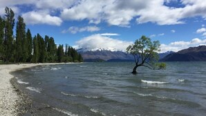 A lake with a tree in the water, surrounded by mountains and a clear sky.