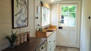 A kitchen with a wooden countertop, a sink, and cabinets. There is a framed bird illustration on the wall and a window with a view of greenery outside.