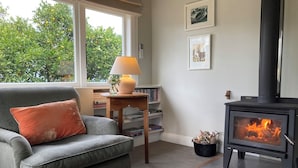 Una sala de estar acogedora con un sillón gris, una mesita con una lámpara, una estantería y una estufa de leña.