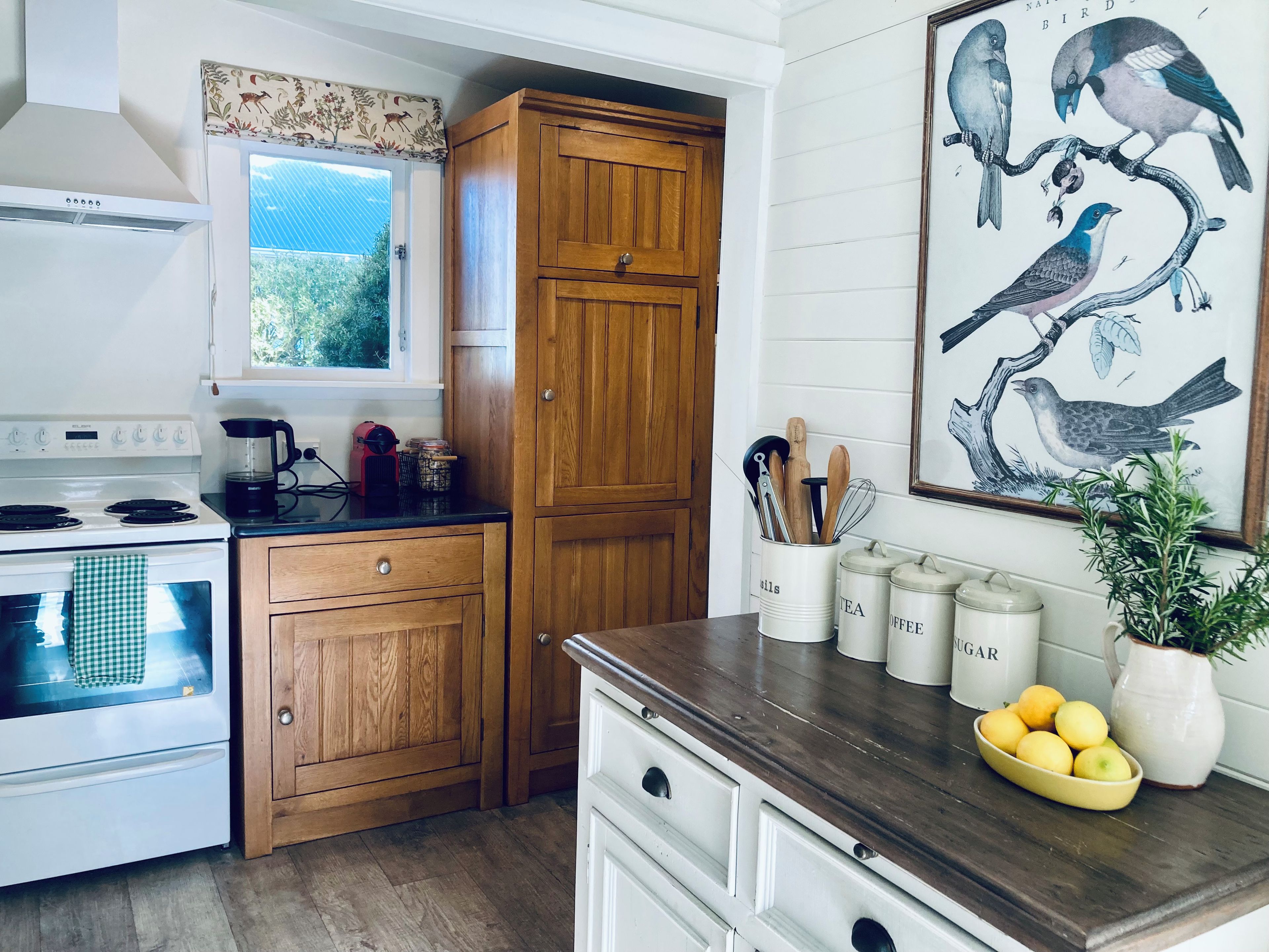A kitchen with wooden cabinets, a stove, a coffee maker, and a painting of birds.