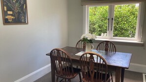 Comedor con mesa y sillas de madera, un jarrón con flores y ventana con vistas al verdor.