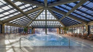 Piscina interna com teto de vidro, cercada por espreguiçadeiras e vista para o exterior.