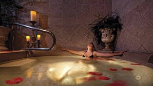 Uma pessoa relaxando em uma banheira de hidromassagem com pétalas de rosas flutuando na água, cercada por velas e um vaso de planta.