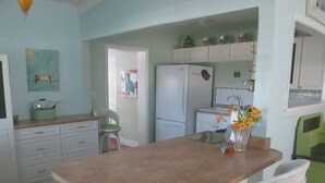 Una cocina con armarios blancos, un refrigerador, un comedor con sillas blancas y una alfombra colorida.