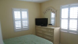 Un dormitorio con cama, cómoda, televisor y ventanas.