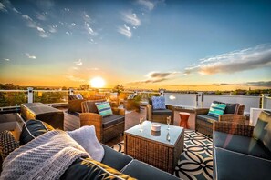 A rooftop terrace with wicker furniture, a coffee table, and a sunset view.