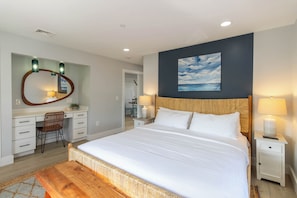 A bedroom with a large bed, a desk, a chair, a nightstand, and a wall-mounted mirror.