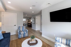 A living room with a sofa, striped armchair, coffee table, and a flat-screen TV mounted on the wall. - Enjoy Sunsets Over Newport Harbor From A Large Roof Deck (Newport)