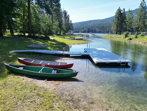 A calm lake with boats docked at a wooden pier, surrounded by trees and a distant mountain range.