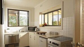 Una cocina moderna con armarios blancos, electrodomésticos de acero inoxidable y amplias ventanas que brindan luz natural.