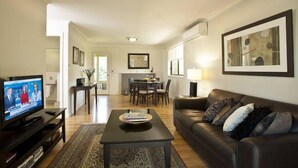Una sala de estar con televisor, sofá, mesa de centro y una zona de comedor al fondo.