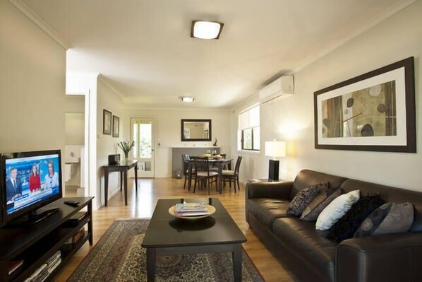 A living room with a television, a sofa, a coffee table, and a dining area in the background.