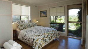 Un dormitorio con cama, mesita de noche, lámpara y ventana con vistas a la vegetación.