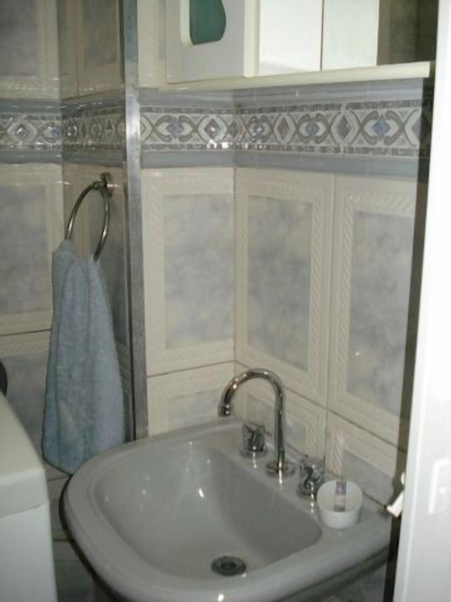Un baño con lavamanos blanco, toallero y baldosas estampadas.