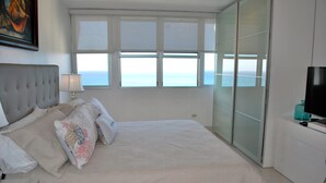 A bedroom with a large bed, a TV, a window with a view of the sea, and a sliding glass door. - Stunning 18th floor remodeled 2/2, beachfront! MONTHLY RENTALS CONSIDERED (Carolina)