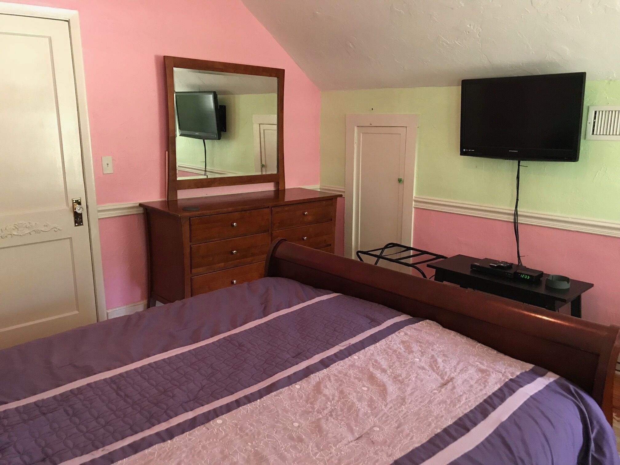 Ein Schlafzimmer mit Bett, Kommode, Spiegel, Fernseher und einer Tür.