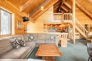 Cozy cabin-style living area with a large sectional sofa, wooden coffee table, and wall-mounted lamp.