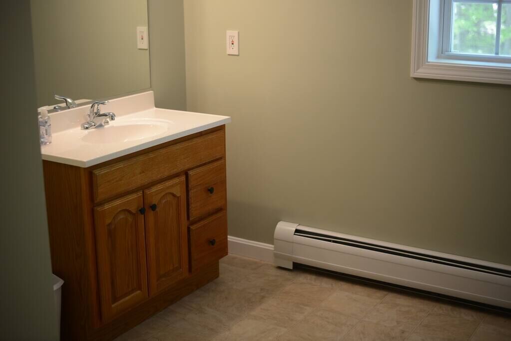 A bathroom with a wooden vanity, a white sink, and a built-in heater.