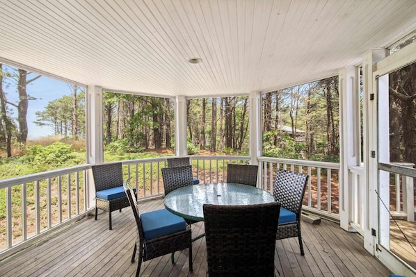 A covered outdoor area with a round glass table and four wicker chairs with blue cushions.