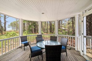 A covered outdoor area with a round glass table and four wicker chairs with blue cushions. - Walk to Private Beach on Lt Island! (Wellfleet)