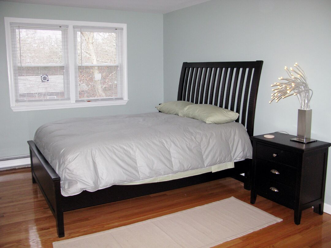 Une chambre à coucher avec un lit, une table de chevet, une lampe et une fenêtre avec des stores.