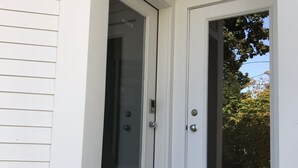 A white door with a glass panel, a blue doormat, and a concrete step leading to the door. - The Art Nook — Renovated 2BR in the Heart of Downtown Bar Harbor (Bar Harbor)