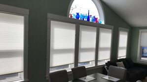A dining area with a table set for four, large windows with blinds, a curved skylight, and a view of the city. - The Art Nook — Renovated 2BR in the Heart of Downtown Bar Harbor (Bar Harbor)