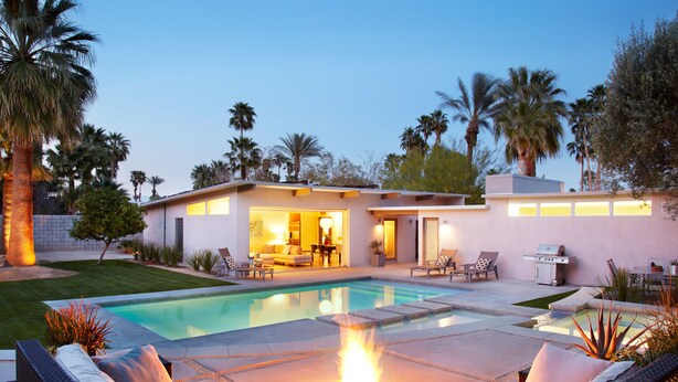 Una casa moderna con piscina, mobiliario exterior y una fogata.