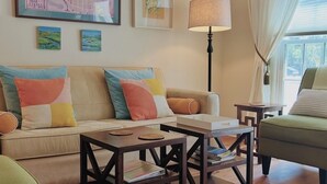 A living room with a sofa, two coffee tables, a floor lamp, and a map on the wall. - Promotions! Stylish Historic District Retreat • Courtyard • Bikes • Walk (Beaufort)