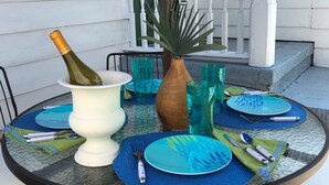 A round glass table set with blue plates, a vase, and a bottle of champagne. - Promotions! Stylish Historic District Retreat • Courtyard • Bikes • Walk (Beaufort)
