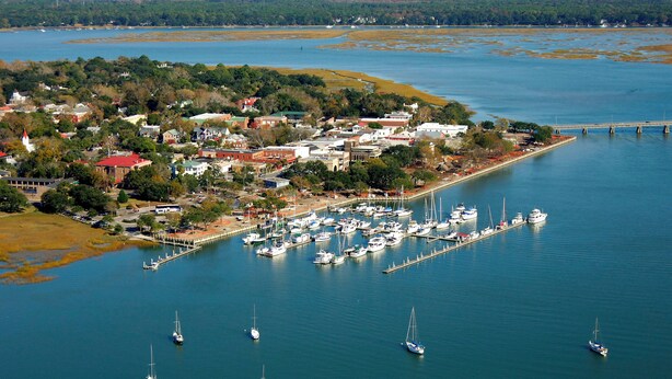 An aerial view of a coastal town with a marina filled with boats, surrounded by residential buildings and a bridge connecting to the mainland. - Promotions! Stylish Historic District Retreat • Courtyard • Bikes • Walk (Beaufort)