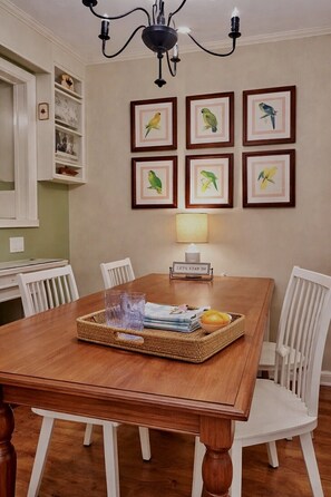 A dining area with a wooden table, white chairs, a chandelier, and framed bird artwork on the wall.