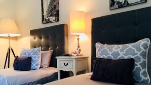 Une chambre d’hôtel avec deux lits, chacun agrémenté de draps à motifs et de coussins décoratifs. On y trouve des tables de chevet avec des lampes et un petit tiroir.