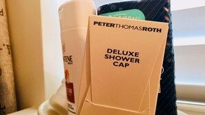 Une salle de bain avec une baignoire blanche, une serviette beige et un bonnet de douche de luxe de la marque Peter Thomas Roth.