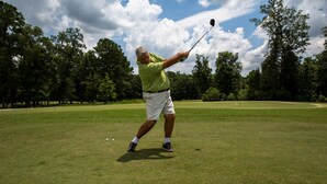 Une personne jouant au golf sur un terrain bien entretenu, avec des arbres en arrière-plan.